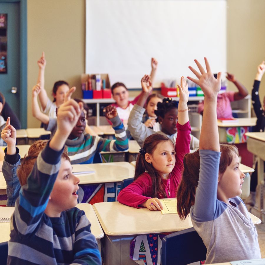 Classroom full of children raising their hands eagerly